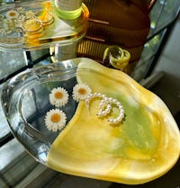 a glass tray with a pair of earrings and daisies on it