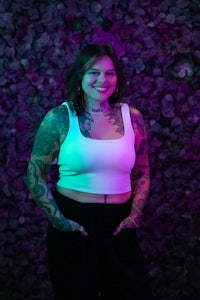 a woman with tattoos standing in front of a purple wall