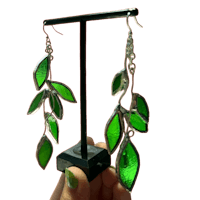 a person is holding up a pair of green leaf earrings