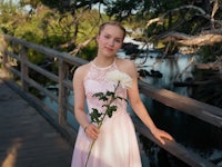 Tytto Koitelin Koskella Oulussa, nojaamassa aitaa vasten mekko päällä, puron ja oksien tausta. Esimerkki Jokakuva valokuvauspalvelusta.