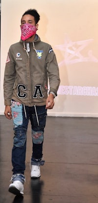 a man walking down the runway with a bandana on his face