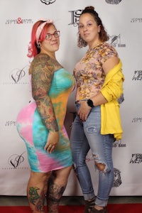 two women with tattoos posing on a red carpet