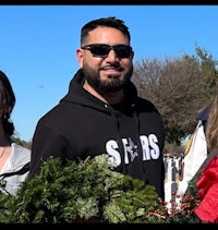 a group of people holding christmas wreaths in front of a cemetery