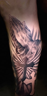 a tattoo of a praying hand with a cross on the leg