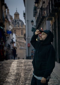 a man in a black hoodie standing on a cobblestone street