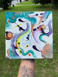 a person holding up an abstract painting in a grassy area