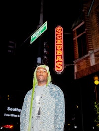 a man in a green hoodie standing in front of a street sign