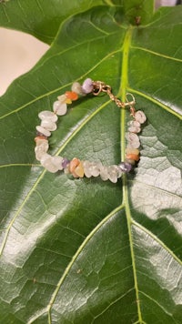 a bracelet with multi colored stones on top of a leaf