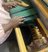a girl is weaving on a wooden loom