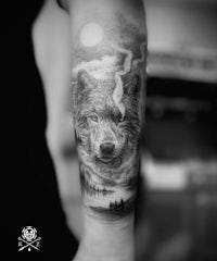 a black and white tattoo of a wolf on the forearm