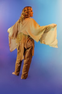 a woman in a tan cloak standing in front of a colorful background