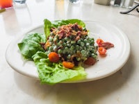 a plate with lettuce, peas and bacon sitting on a table