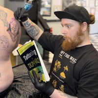 a man tattooing a man's back with a book