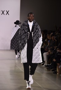 a man walking down the runway in a black and white coat