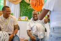 two men laughing while holding balloons at a baby shower