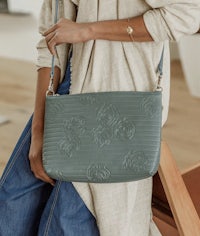 a woman is holding a green cross body bag