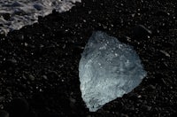 a piece of ice sitting on a black sand beach