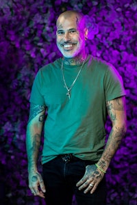 a man with tattoos standing in front of a purple wall