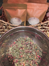 a bowl full of dried flowers and herbs next to a bag of tea