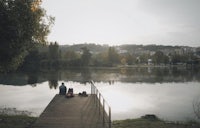two people sitting on a dock near a lake