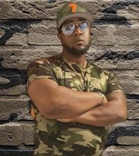 a man in a camouflage shirt standing in front of a brick wall