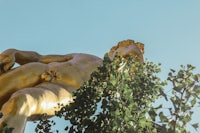 a golden statue of a man with a shaved head on top of a tree
