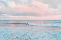 a group of people are surfing in the ocean at sunset