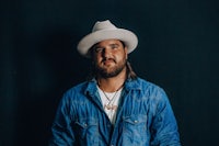 a man in a hat and jeans poses for a photo