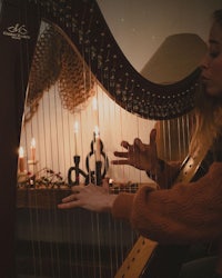 a woman playing a harp in front of candles