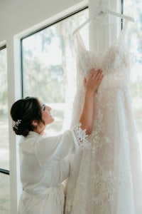 a bride putting on her wedding dress in front of a window