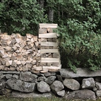 a pile of wood is stacked against a stone wall
