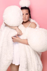 a woman in a white fur coat posing on a pink background