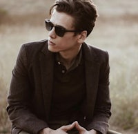 a young man in sunglasses sitting in a field