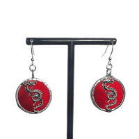 a pair of red and silver earrings on a metal stand