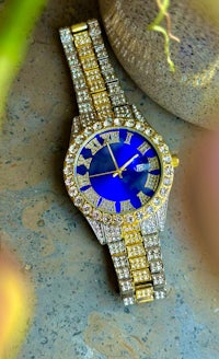 a gold and blue watch on a table next to a flower