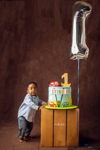 a boy standing next to a cake with a balloon