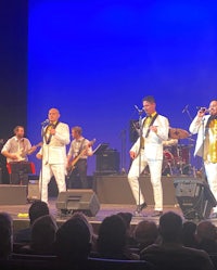 a group of men in white suits singing on stage