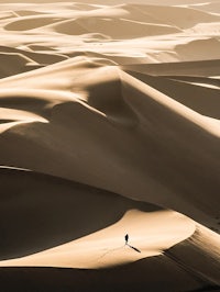 a man walking across a sand dune in the desert