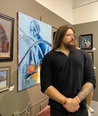a man standing in front of paintings in an art gallery