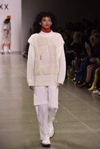 a model walks down the runway wearing a white sweater and white pants