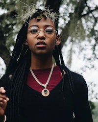 a woman with dreadlocks and glasses standing in a tree