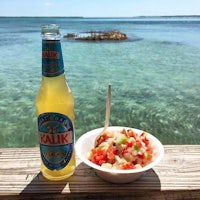 a bottle of beer and a bowl of salsa next to the ocean