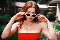 a young woman in a red dress is holding a pair of sunglasses