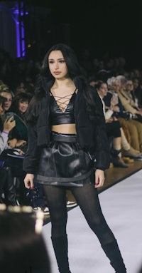 a woman walking down the runway in a black outfit