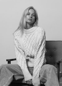 a black and white photo of a woman in a white sweater sitting on a chair