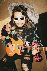 a man with sunglasses and a guitar sitting on a couch