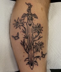 a tattoo of a sword with flowers on it