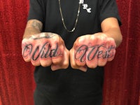 a man's hands with the word wild west tattooed on them