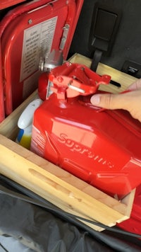 a person holding a red gas can in the trunk of a car