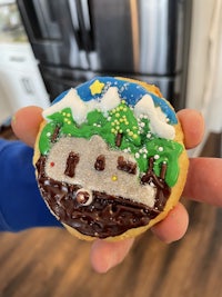 a person is holding a cookie decorated with a house